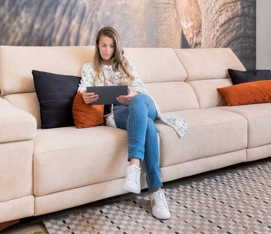 Mujer sentada en sofá con tableta, relajada en casa.